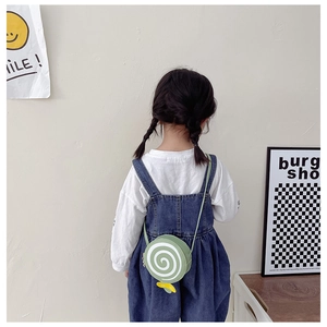 Girl in denim overalls wearing a green lollipop-shaped shoulder bag with yellow bow