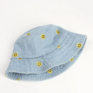 Detail of light blue denim bucket hat featuring embroidered yellow smiley faces
