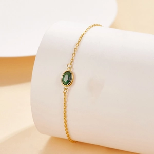 Close-up of gold chain bracelet featuring a bezel-set oval green gemstone on a display stand