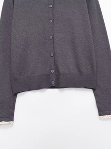 Détail du cardigan gris foncé avec fermeture à boutons et poignets en dentelle blanche