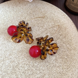 Detail of vintage acrylic leopard flower earrings with red beads on a ceramic tray