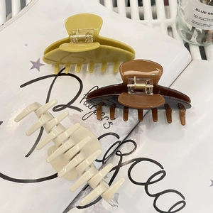 Drei Haarklammern aus Acetat in Gelb, Braun und Beige auf einem Buch bei sanftem Licht