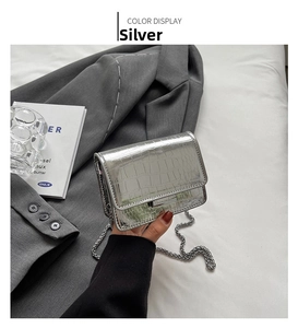 Close-up of silver crocodile embossed crossbody bag with metallic chain strap and glossy finish