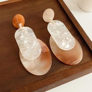 Detail view of acrylic geometric earrings with white marble and orange-brown resin texture