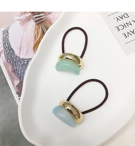 Close-up of minimalist hair ties with gold metal and resin charms on ceramic tray