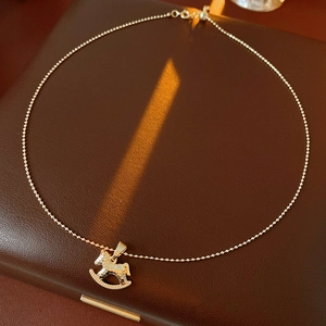 Détail macro du collier pendentif cheval à bascule doré sur une surface en cuir