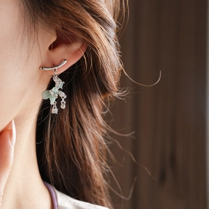 Close-up of model wearing silver bow earrings with light green tassel and zircon