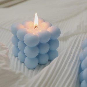 Blue bubble cube scented candle with a burning flame on a minimalist white fabric background
