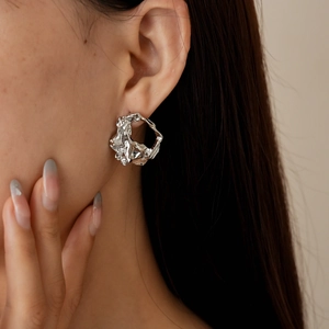 Close-up of geometric wrinkled silver earrings on model featuring hollow metal texture