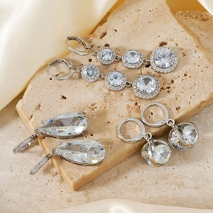 Three-piece silver earrings set with zircon stones on a beige textured stone background