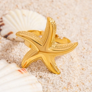 Elegant gold starfish ring with textured detail on white beach sand with sea shells