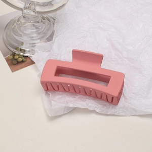 Close-up of pink matte rectangular hair claw clip on white textured paper background