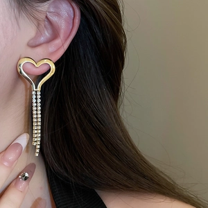 Model wearing gold heart tassel drop earrings with sparkling rhinestones in a macro shot