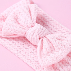 Macro detail of pink knit baby headband showing soft waffle texture and large bow decoration
