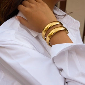 Polished double-layered gold wide bangle bracelet set worn by a model in a white shirt