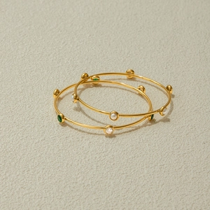Dettaglio di bracciali in acciaio inossidabile 18K con perle bianche e pietre verdi