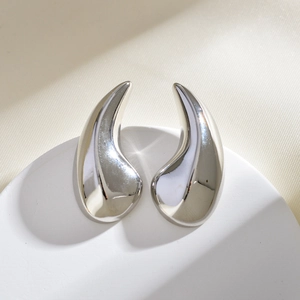 Detailed close-up of polished silver teardrop earrings on a white round pedestal