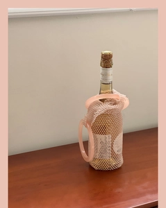 Detail of pink hand-woven beaded mesh bag holding a champagne bottle with round handles