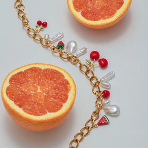 Detail view of gold chunky chain bracelet with cherry, strawberry and pearl charms
