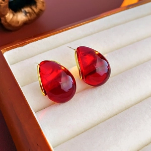 Macro shot of French style pear-shaped red resin earrings on beige jewelry box