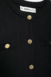 Close-up of knit cardigan neckline featuring golden embossed buttons and size label