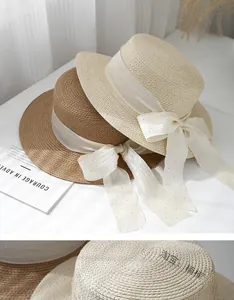 Flat top straw sun hats in beige and khaki with sequined bow ribbons on a white surface