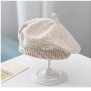 Detail view of a beige knitted baby beret featuring textured patterns and top stem decoration