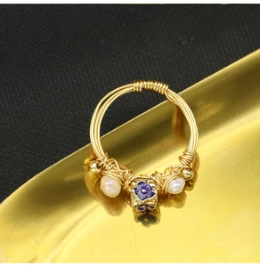 Macro detail of a woven gold ring with natural pearls and purple flower bead