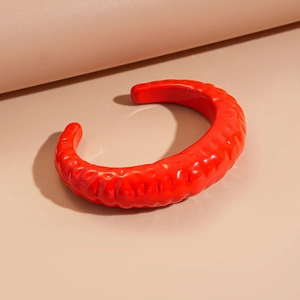 Dettaglio del bracciale aperto in acrilico rosso con trama a pieghe e finitura lucida