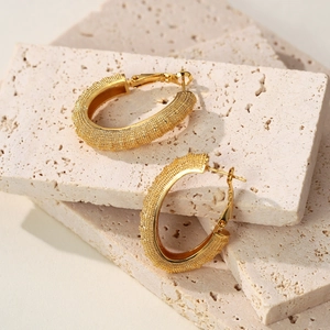 Minimalist matte gold hoop earrings with grainy texture on ivory stone base