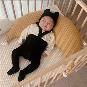 Detail of baby in knitted outfit resting on a yellow crescent moon nursing pillow