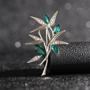 Elegant gold bamboo brooch featuring green gemstones and white rhinestones on dark background