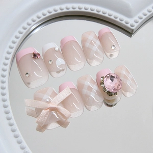Pink and white press-on nails with plaid pattern, heart gems and a large fabric bow