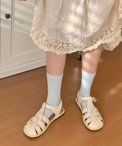 Détail de sandales tressées crème avec chaussettes bleues sur parquet style vintage