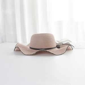 Detail of pink straw sun hat with wavy brim and black polka dot ribbon bow decoration