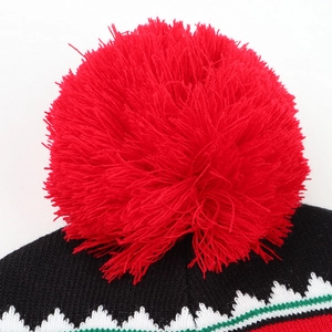 Close-up of a large red pom-pom and festive knitted pattern on a winter elk beanie