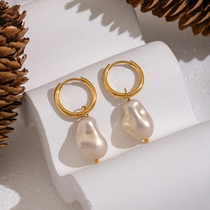 Close-up of irregular Baroque pearl drop earrings on a golden metal hoop display
