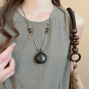 Detail view of a vintage dark wood bottle pendant on a white cord with wooden beads