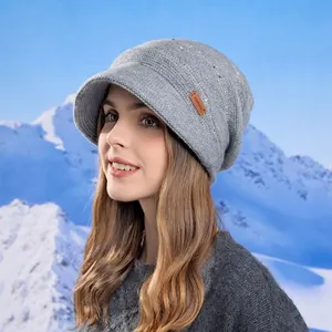 Grey winter knit hat with brim and ear protection, styled against a snowy mountain backdrop