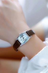 Close-up of a square silver watch with brown leather strap and Roman numeral dial on wrist
