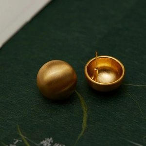 Detail view of gold matte finish ball earrings showing brushed texture and hollow structure