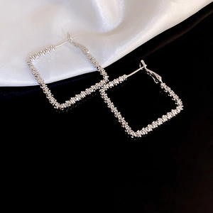 Macro detail of silver U-shaped earrings with crushed silver texture on white silk