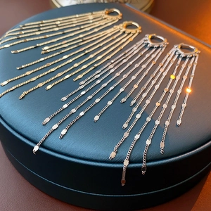 Detail of gold and silver tassel chain earrings with sequins on a green jewelry box