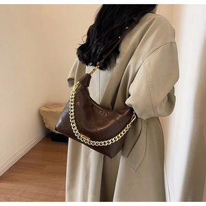 Close-up of deep brown quilted crossbody bag with gold chain strap on a model