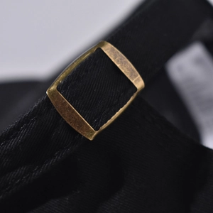 Detailed close-up of retro bronze metal slider on black cotton twill baseball cap strap
