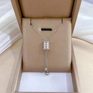 Macro detail of silver tassel cylinder pendant necklace in a beige jewelry box