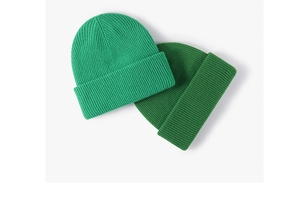 Close-up of two green ribbed knit wool beanies showing fine texture and shades
