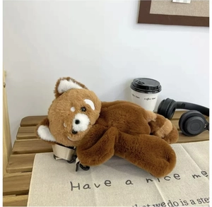 Detail of red panda plush backpack with beige adjustable strap on a cozy wooden bench
