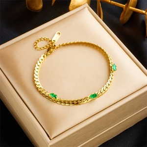 Elegant gold titanium steel bracelet with emerald-cut green gems on a brushed metal box