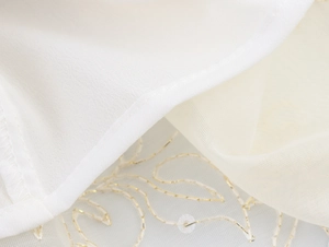 Macro d'un tissu blanc avec tulle translucide brodé d'or sur une robe élégante